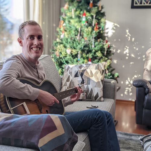 Lucas Silbernagel sitting on a couch playing an acoustic guitar